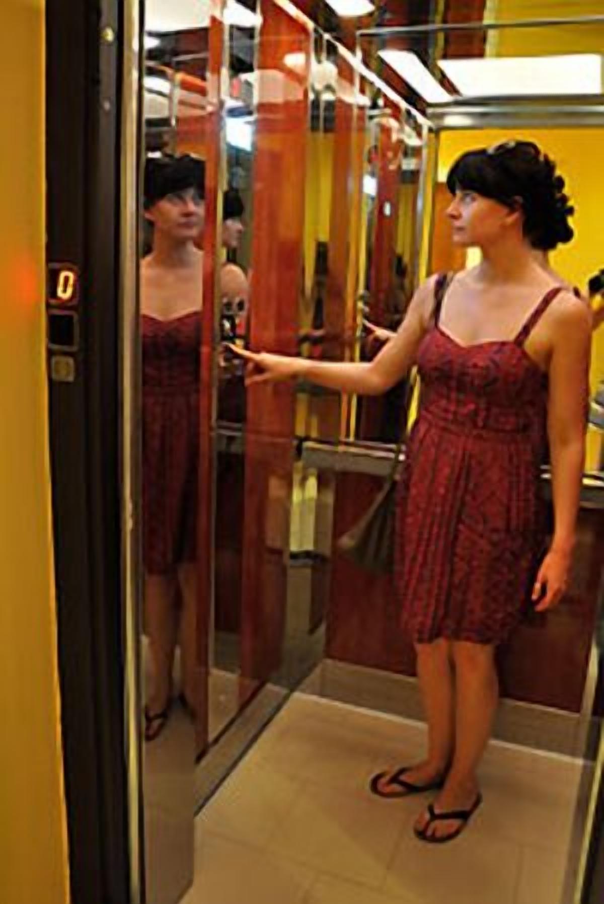 A woman in a red dress standing in an elevator with a mirror on the wall.