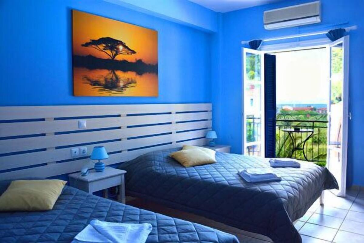 A bedroom with two beds, a nightstand, a painting of a tree, and a balcony with a view.