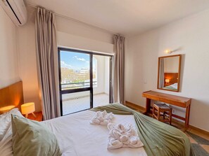 A hotel room with a bed, a desk, a chair, a lamp, and a large window with curtains.