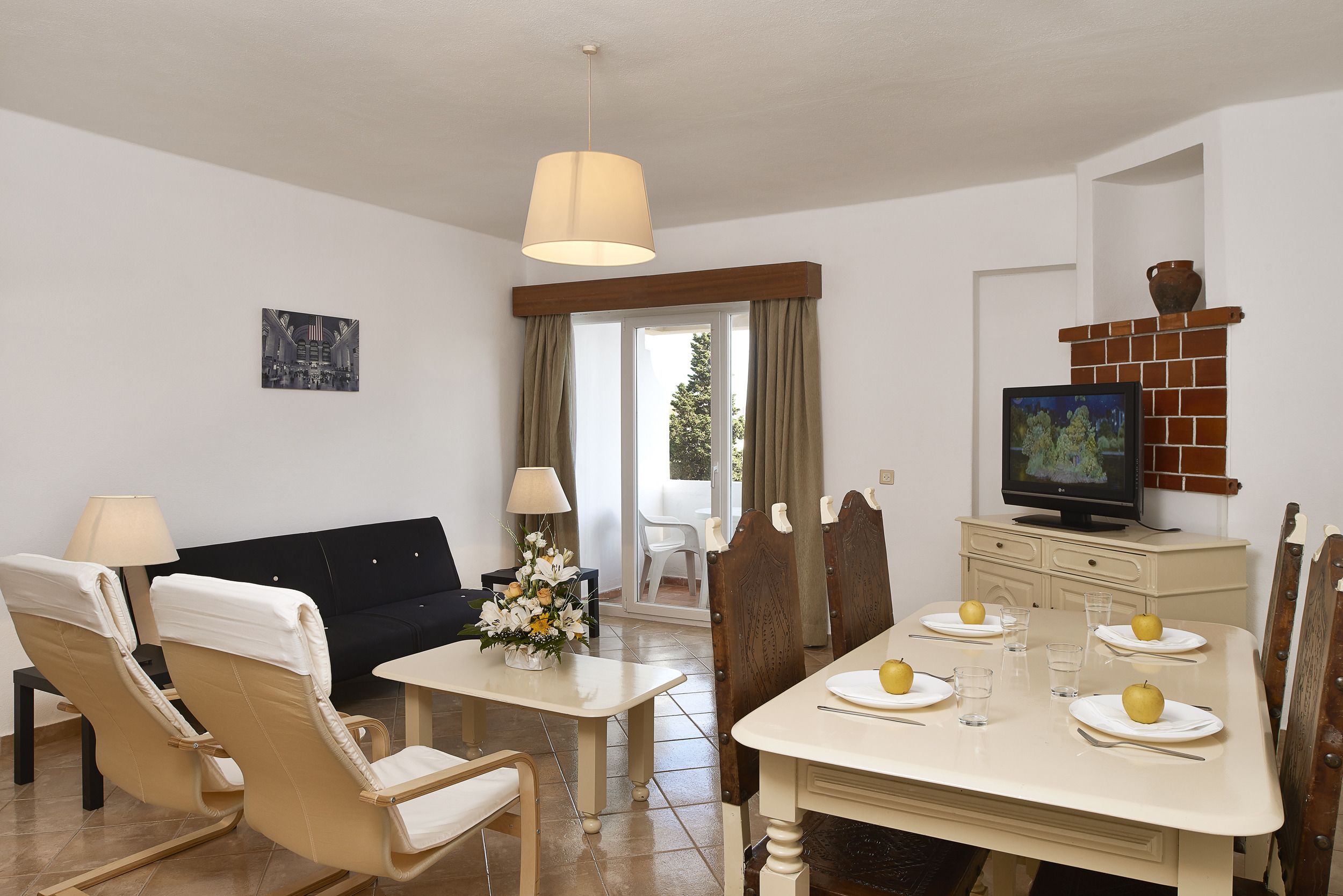 Un comedor con una mesa dispuesta para cuatro, un sofá y un televisor sobre un mueble.