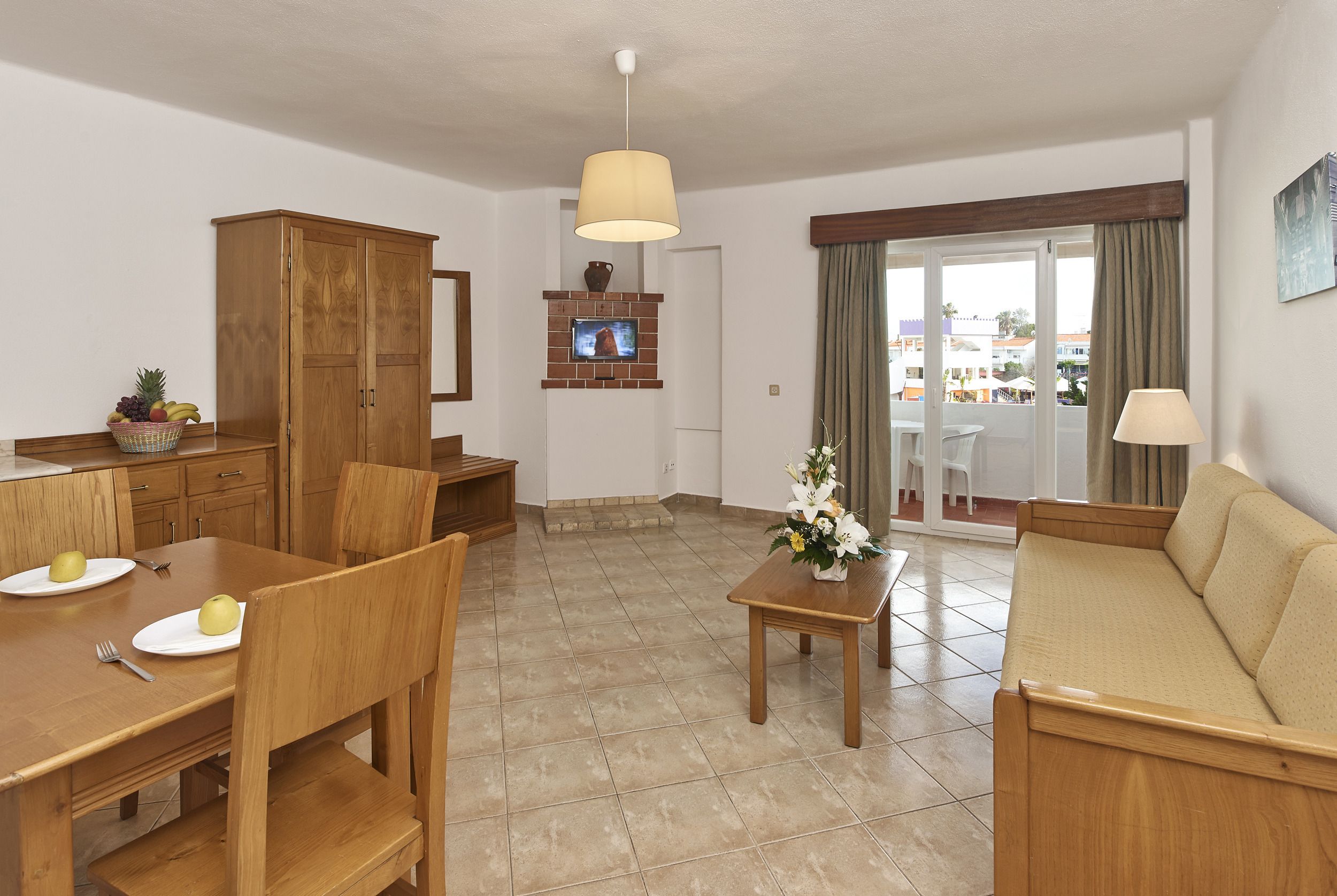 A spacious living area with a wooden dining table, chairs, a sofa, and a TV mounted on a brick fireplace.