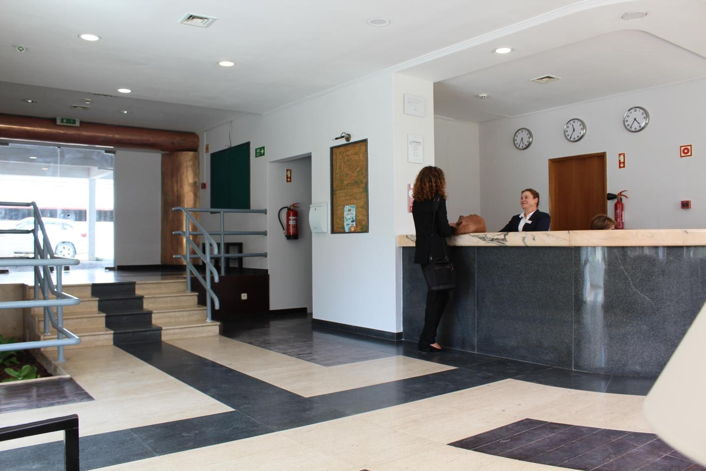 Un área de recepción con mostrador, escalera y extintor en la pared.