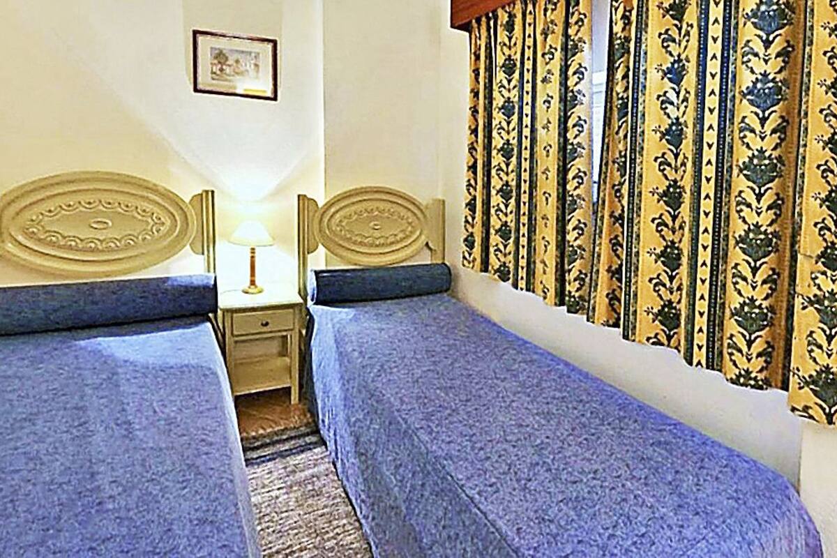 Una stanza con due letti singoli, un comodino con una lampada, tende a motivi decorativi e un quadro appeso al muro.