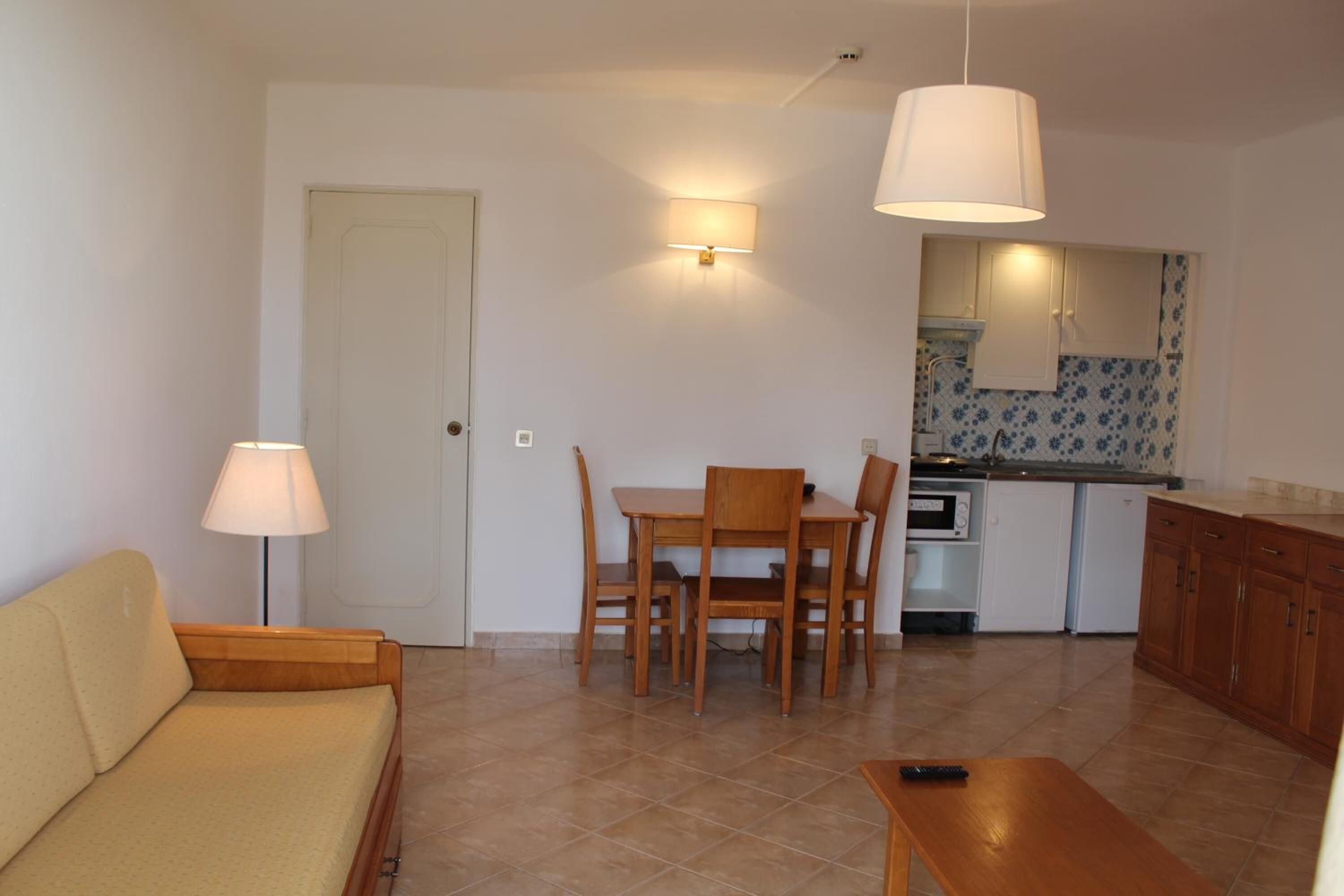 A compact living space with a sofa, dining table, chairs, a kitchen area, and a door.