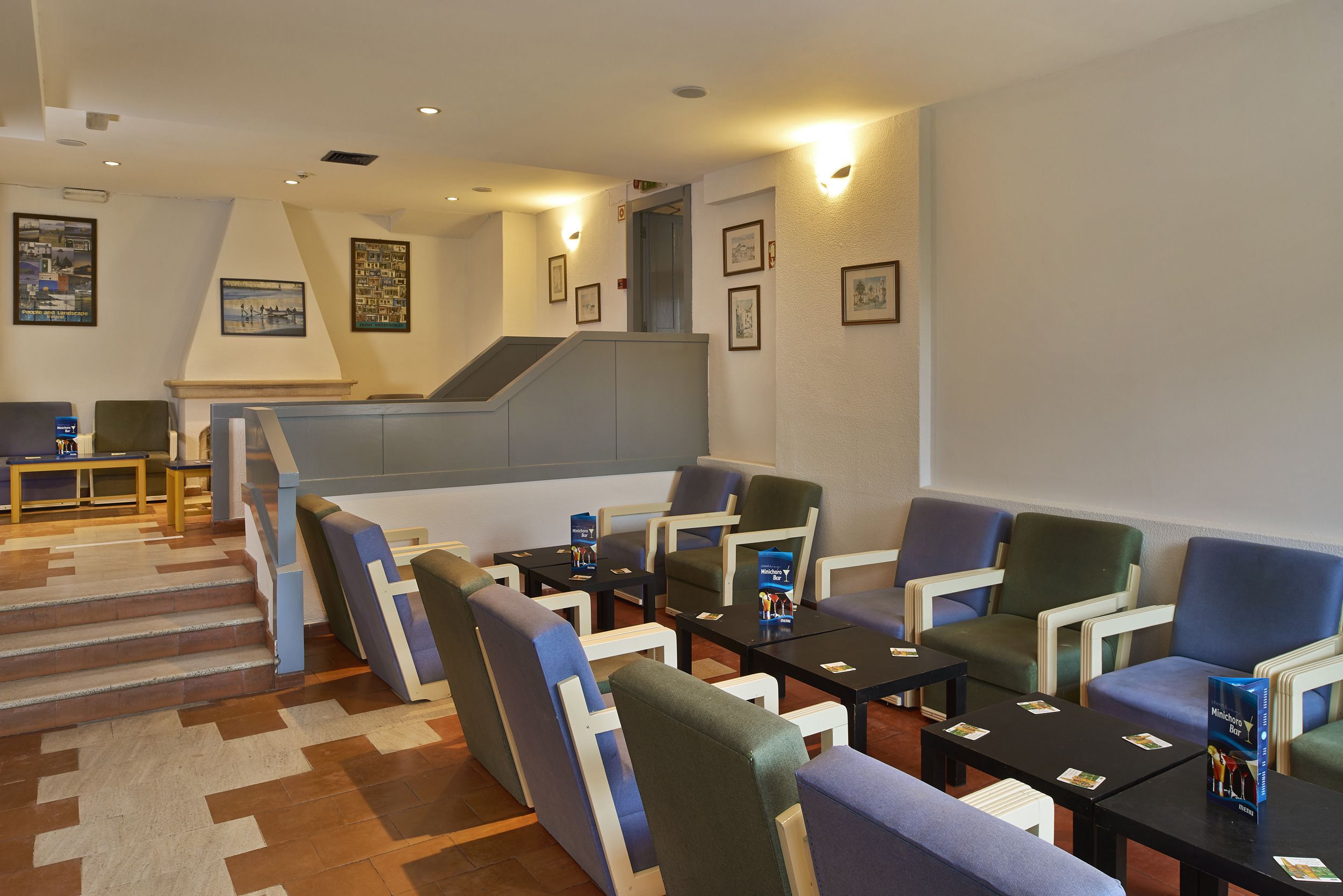A hotel lobby with a staircase, seating area, and framed pictures on the walls.