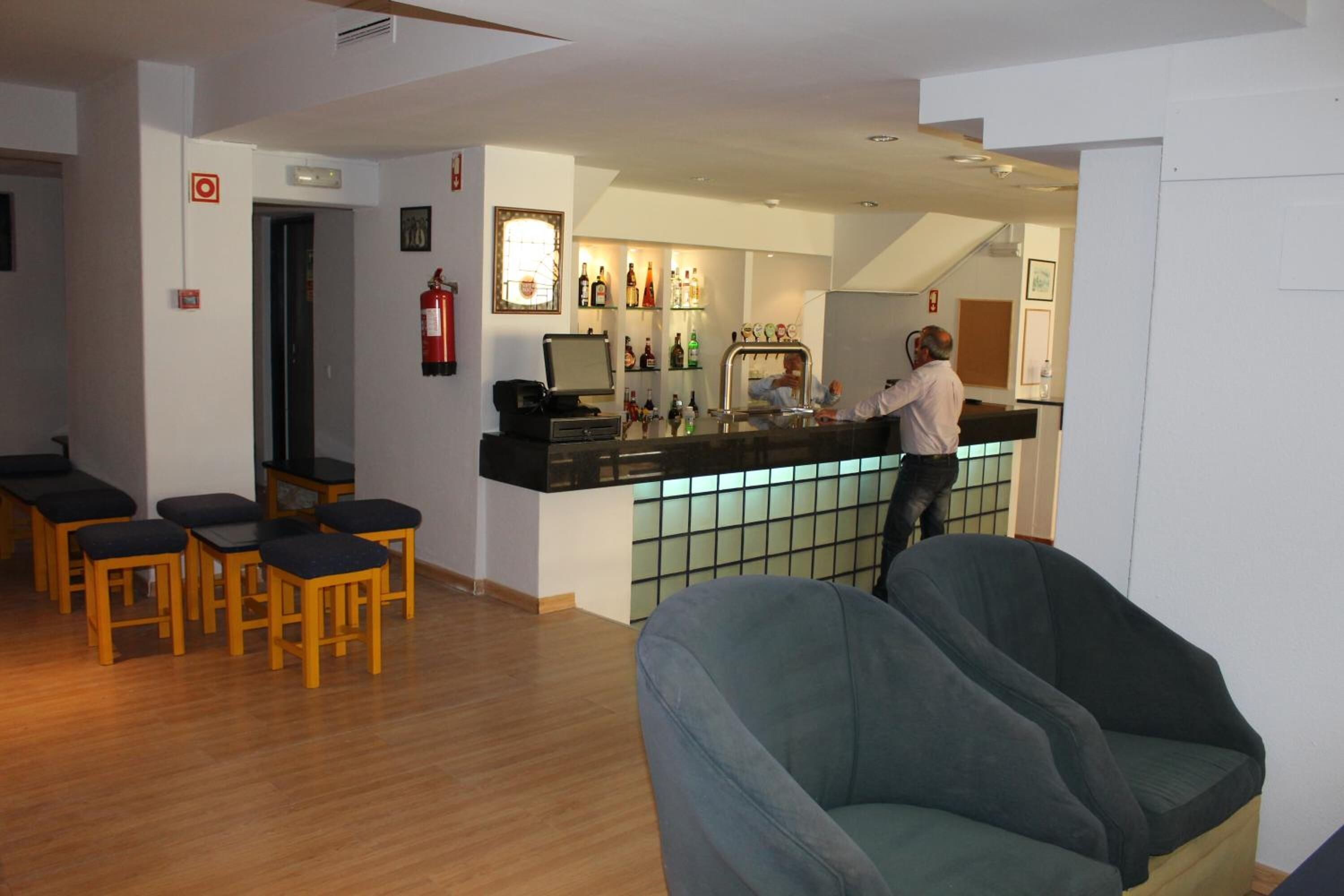 A bar area with a bartender, wooden chairs, and a counter with various bottles.