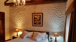 A bedroom with a textured white wall, a wooden ceiling, a bed with white bedding, two bedside lamps, and a framed picture on the wall. - Quito Antiguo (Quito)