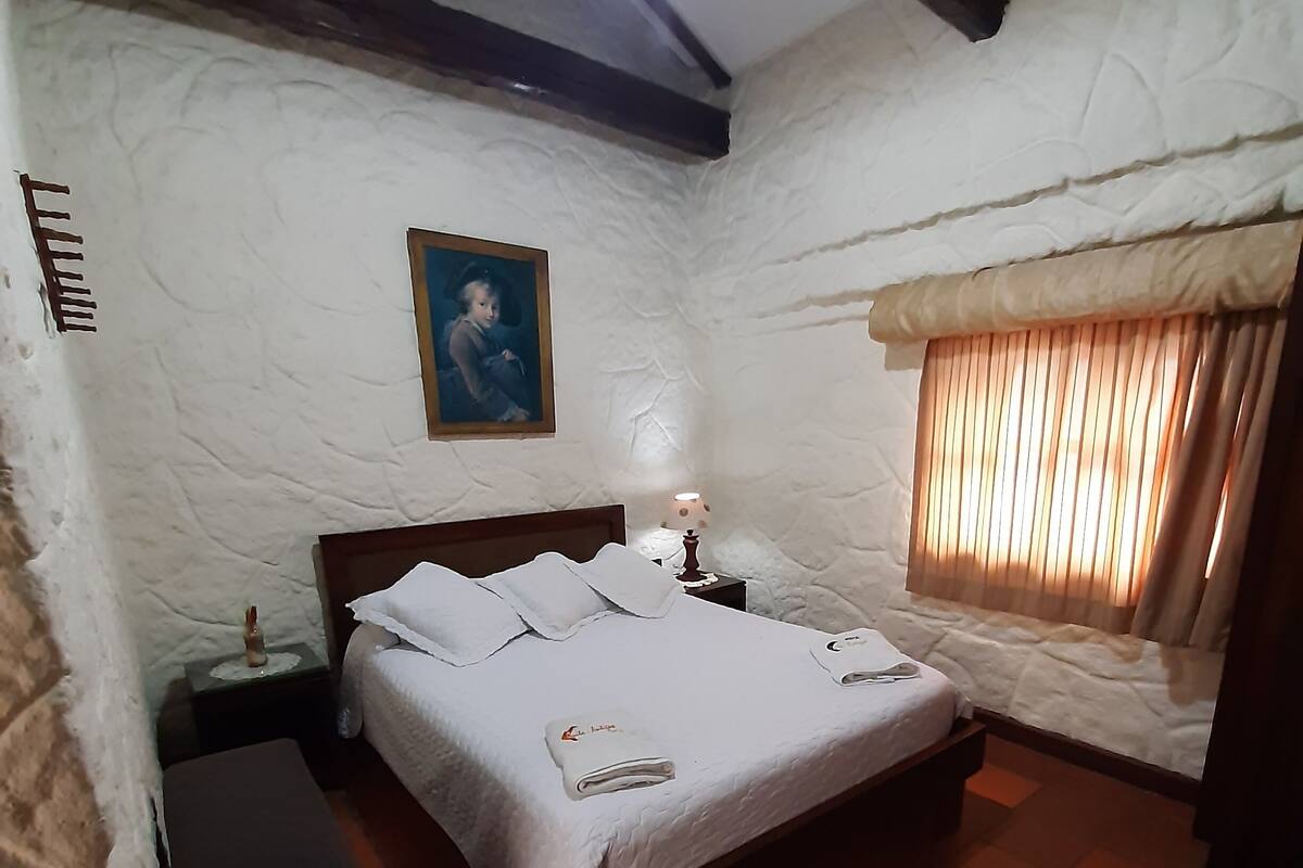 A bedroom with a bed, bedside table, lamp, and a window with curtains.