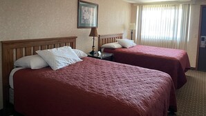 Habitación de hotel con dos camas, cada una con cabecero de madera y ropa de cama roja. Hay un cuadro enmarcado en la pared, una lámpara en la mesita de noche y una ventana con cortinas.