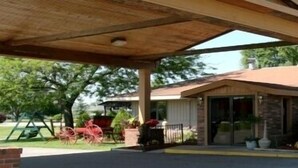 Un espacio al aire libre cubierto con la entrada de un edificio, un conjunto de columpios y un carrete rojo estacionado.