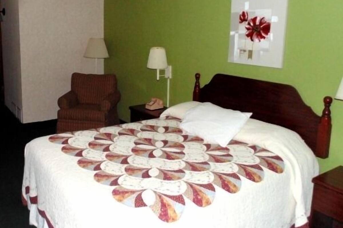 Quarto de hotel com cama, cadeira, mesa de cabeceira, abajur e decoração na parede.