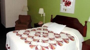 A hotel room with a bed, a chair, a nightstand, a lamp, and a wall decoration.