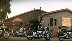 Una fila de motocicletas estacionadas frente a un edificio con un letrero que dice 'BENCH'.