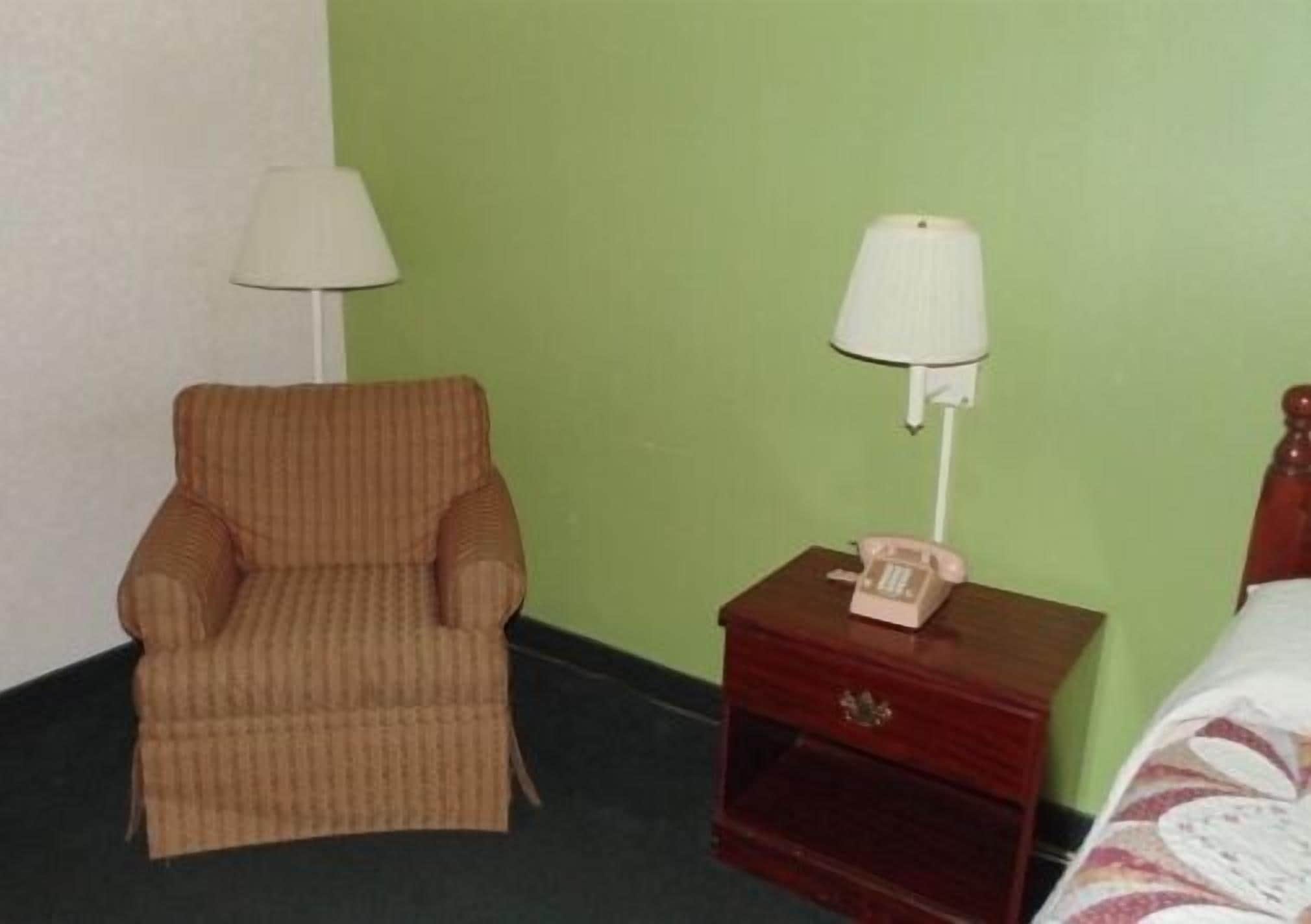 A room with a striped armchair, a bedside table with a lamp, and a telephone.