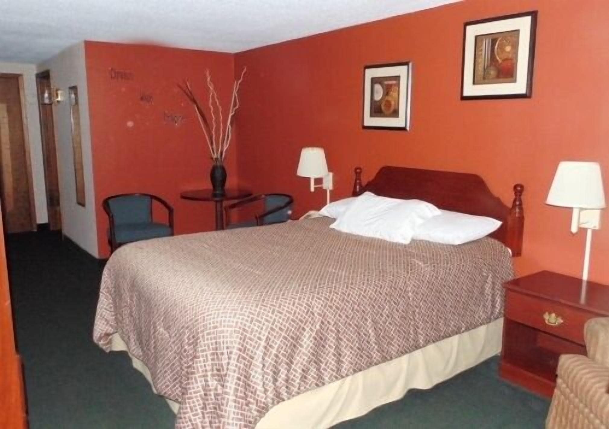 A hotel room with a bed, two bedside tables, a chair, a small table, and two lamps.