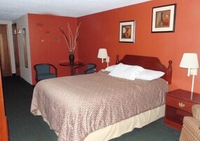 A hotel room with a bed, two bedside tables, a chair, a small table, and two lamps.