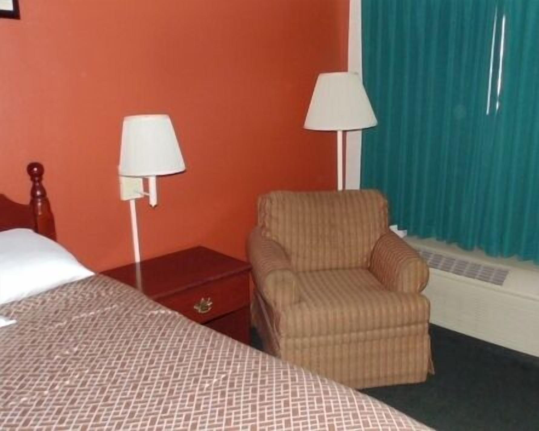 Une chambre d’hôtel avec un lit, une chaise, une table de chevet et une lampe.