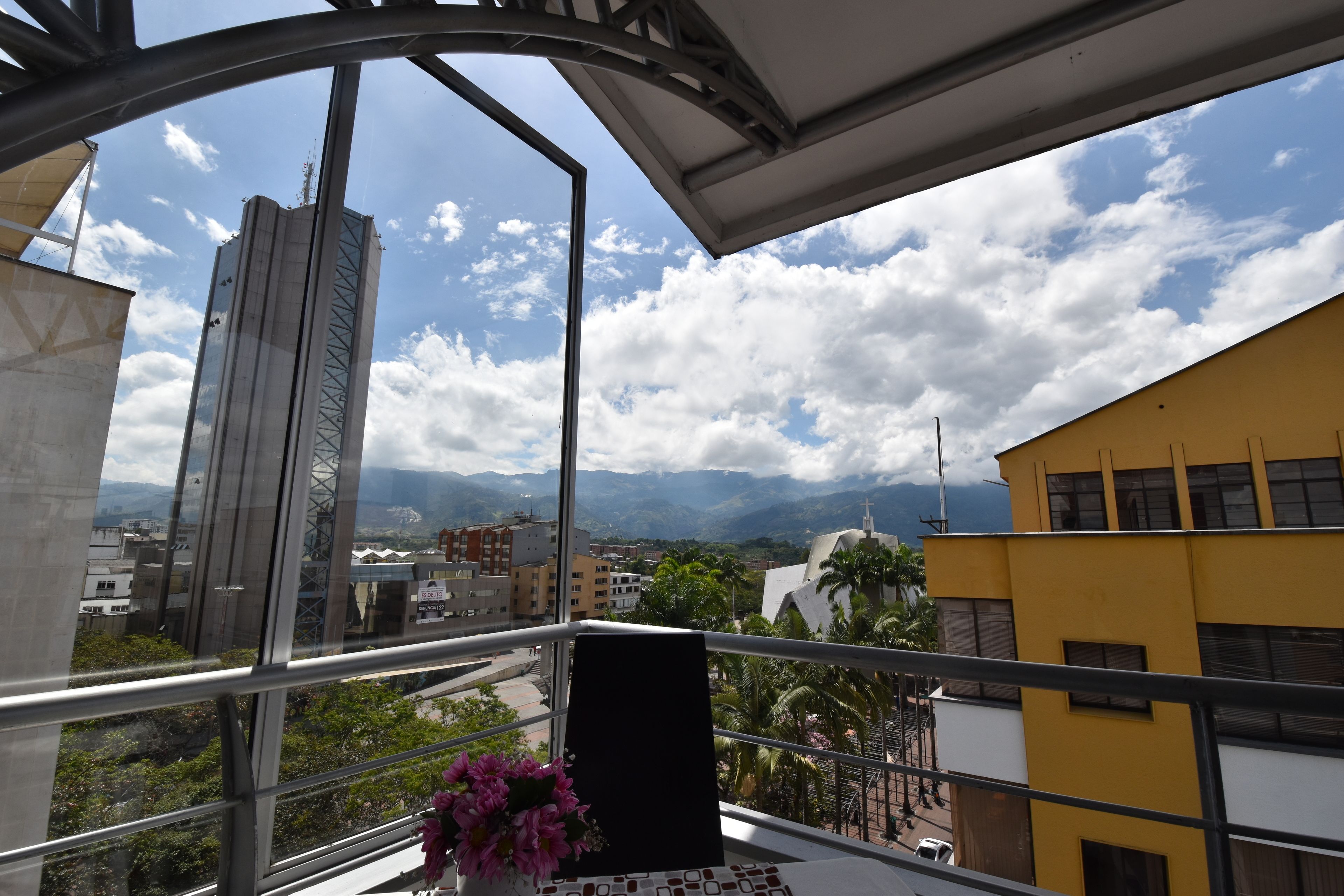 Un balcón con vista a un paisaje urbano, que incluye un edificio alto y montañas al fondo.