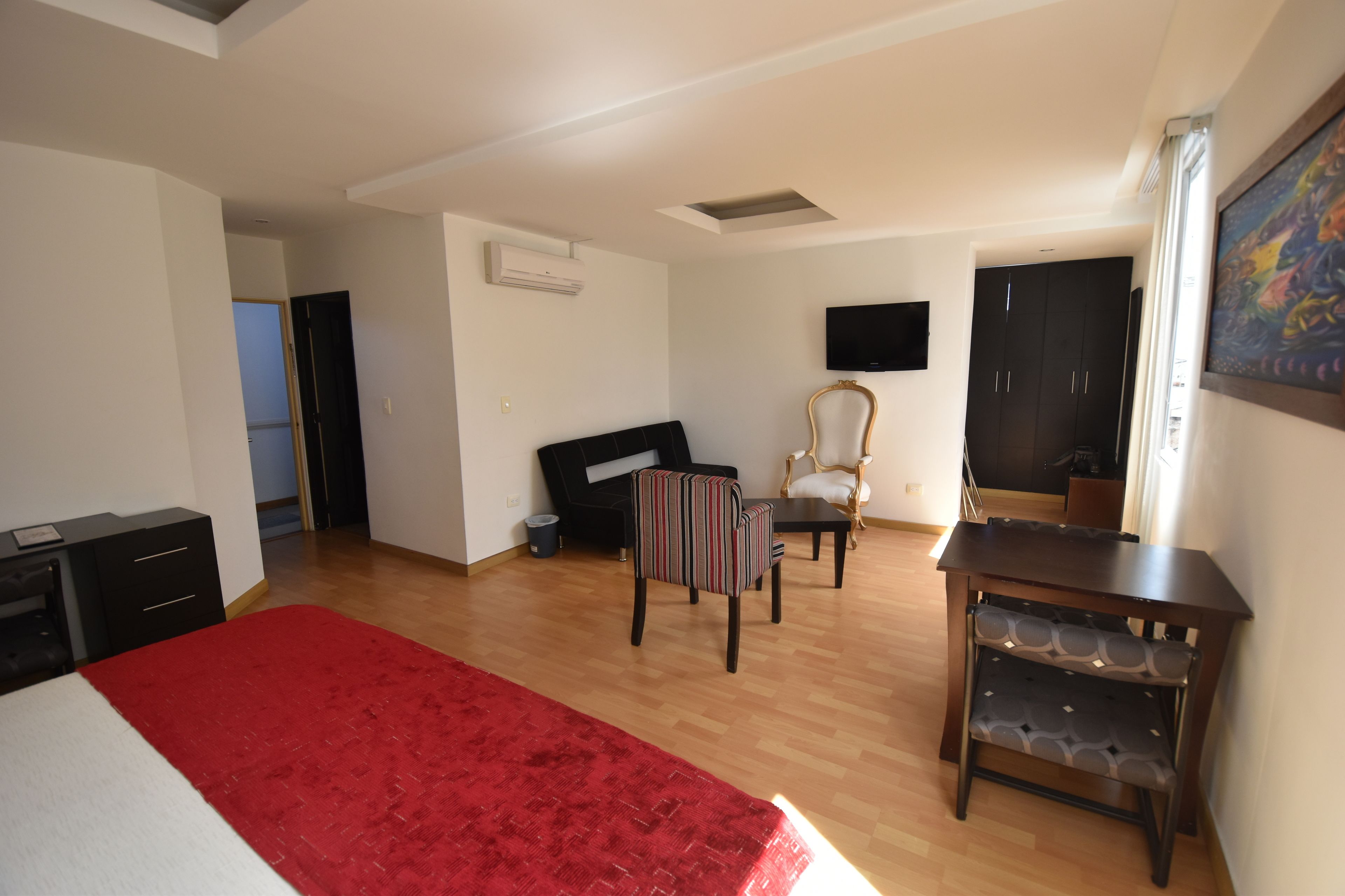 Un dormitorio con cama, una alfombra roja, escritorio, silla, televisor y armario.