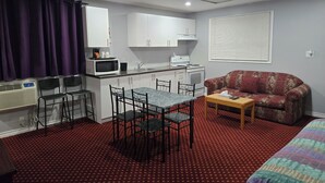 A compact room with a kitchenette, a dining area with a table and chairs, a sofa, and a bed. - Cobourg Inn (Hamilton Township)