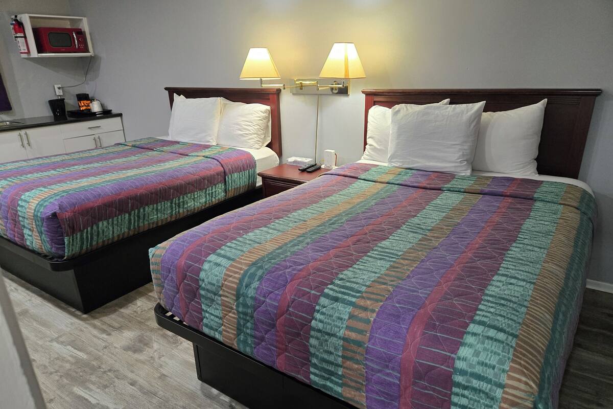 Zwei Betten mit bunten Quilts, ein Nachttisch mit Lampe und eine Mikrowelle über einer kleinen Küchenzeile.