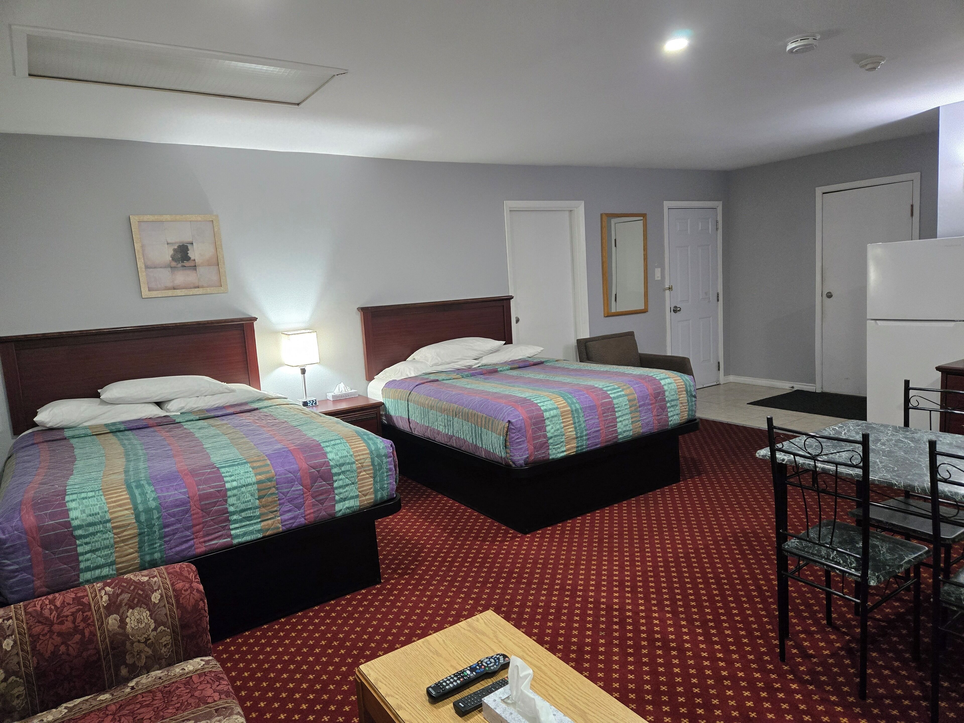 Habitación de hotel con dos camas, un escritorio, una silla, un refrigerador y un televisor.