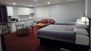 A hotel room with a kitchenette, two beds, a dining area with chairs, and a patterned carpet. - Cobourg Inn (Hamilton Township)