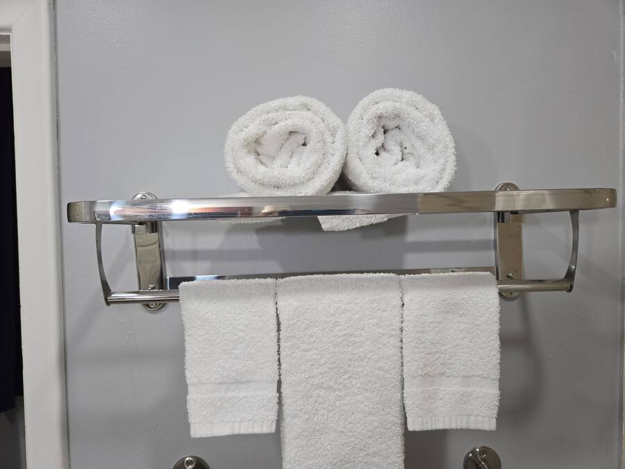 Un baño con un perchero que sostiene dos toallas enrolladas y dos toallas dobladas.