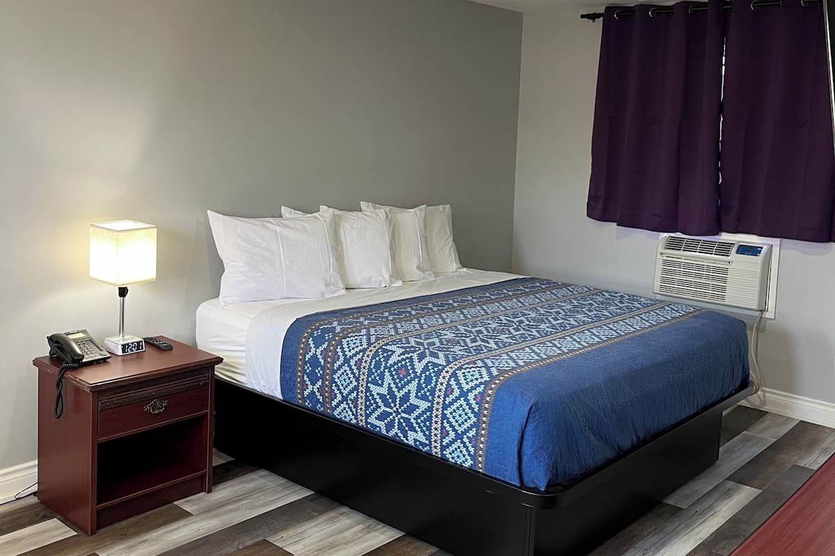 Ein Hotelzimmer mit Bett, Nachttisch, Lampe, Klimaanlage und Deckenleuchte.