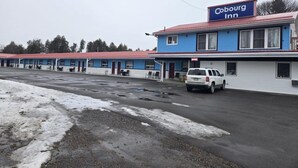 A Cobourg Inn with a red roof and blue exterior walls, featuring a parking lot and a white vehicle parked in front. - Cobourg Inn (Hamilton Township)
