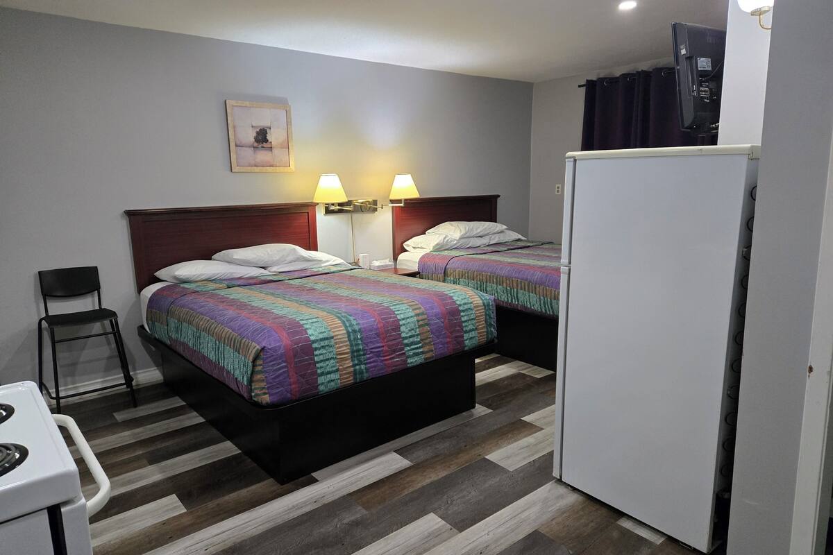 Ein Hotelzimmer mit zwei Betten, einer kleinen Küchenzeile, einem Sessel und einem Kühlschrank.