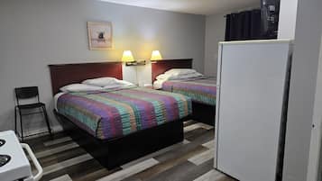 A hotel room with two beds, a small kitchenette, a chair, and a refrigerator.