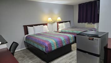 Hotellihuone, jossa on kaksi sänkyä, työpöytä, jääkaappi ja ikkuna, jossa on verhot.