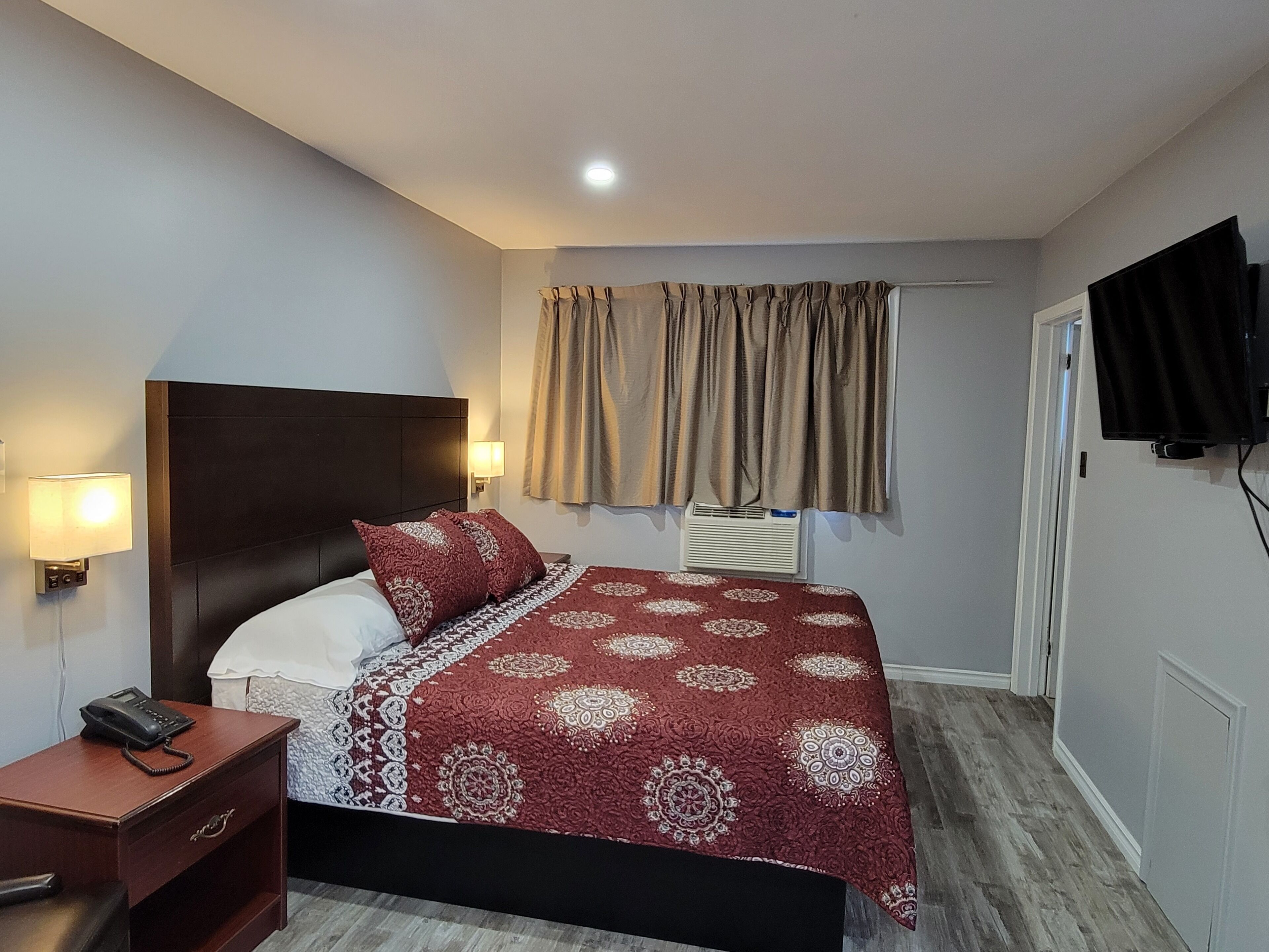 A hotel room with a bed, bedside table, lamp, and a television mounted on the wall.
