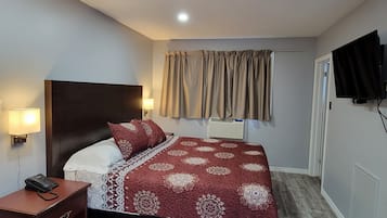 A hotel room with a bed, bedside table, lamp, and a television mounted on the wall.