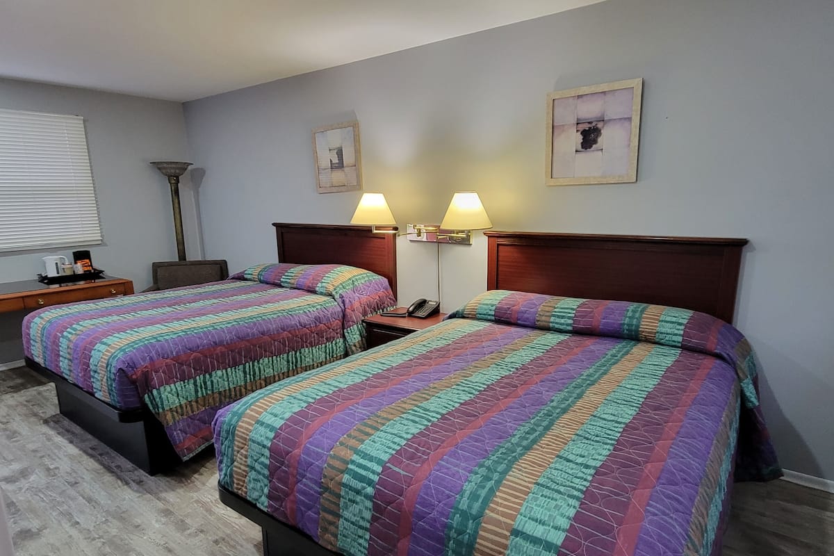 Ein Hotelzimmer mit zwei Betten, jedes mit einer farbenfrohen Steppdecke, einem Nachttisch mit Lampe und einem kleinen Tisch mit Kaffeemaschine.