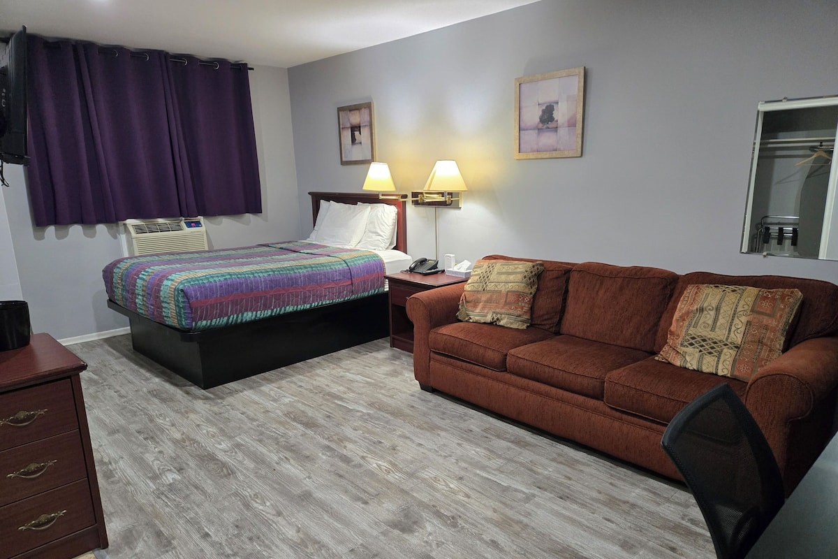 Ein Schlafzimmer mit einem Bett, einem braunen Sofa, einem Nachttisch, einer Lampe und einer Wandklimaanlage.