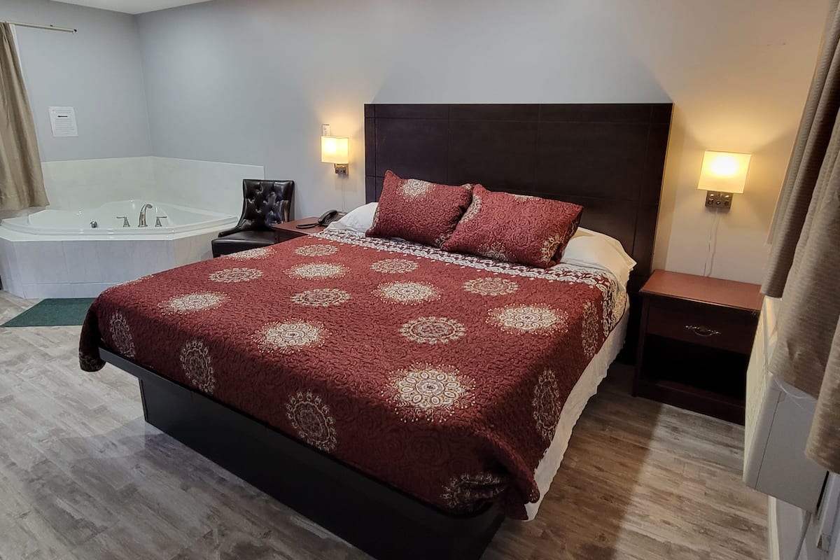 Ein Hotelzimmer mit einem großen Bett, einem eigenen Badezimmer mit Badewanne und zwei Nachttischen mit Lampen.
