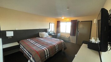 Habitación de hotel con cama, escritorio, silla, televisor y ventana con cortinas.