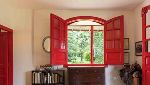 Una habitación con un gran ventanal arqueado, una estantería, un aparador de madera y una puerta roja.