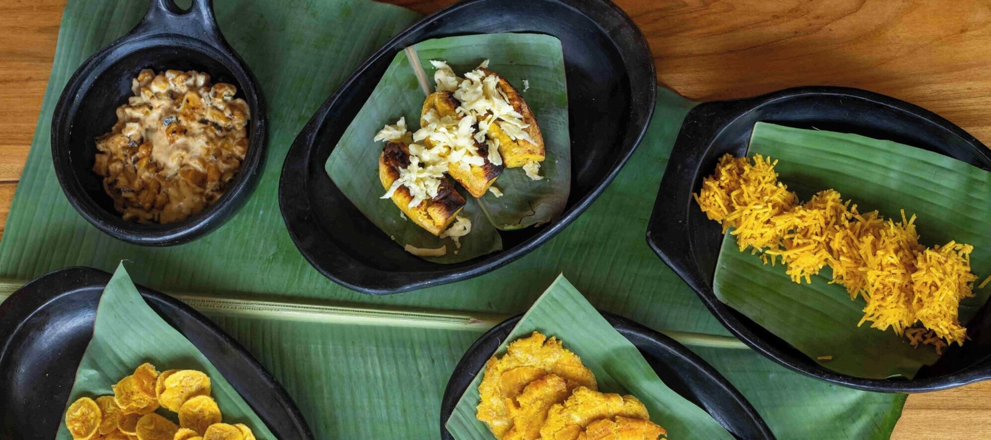 A table with four black bowls containing different dishes, each served on a banana leaf.