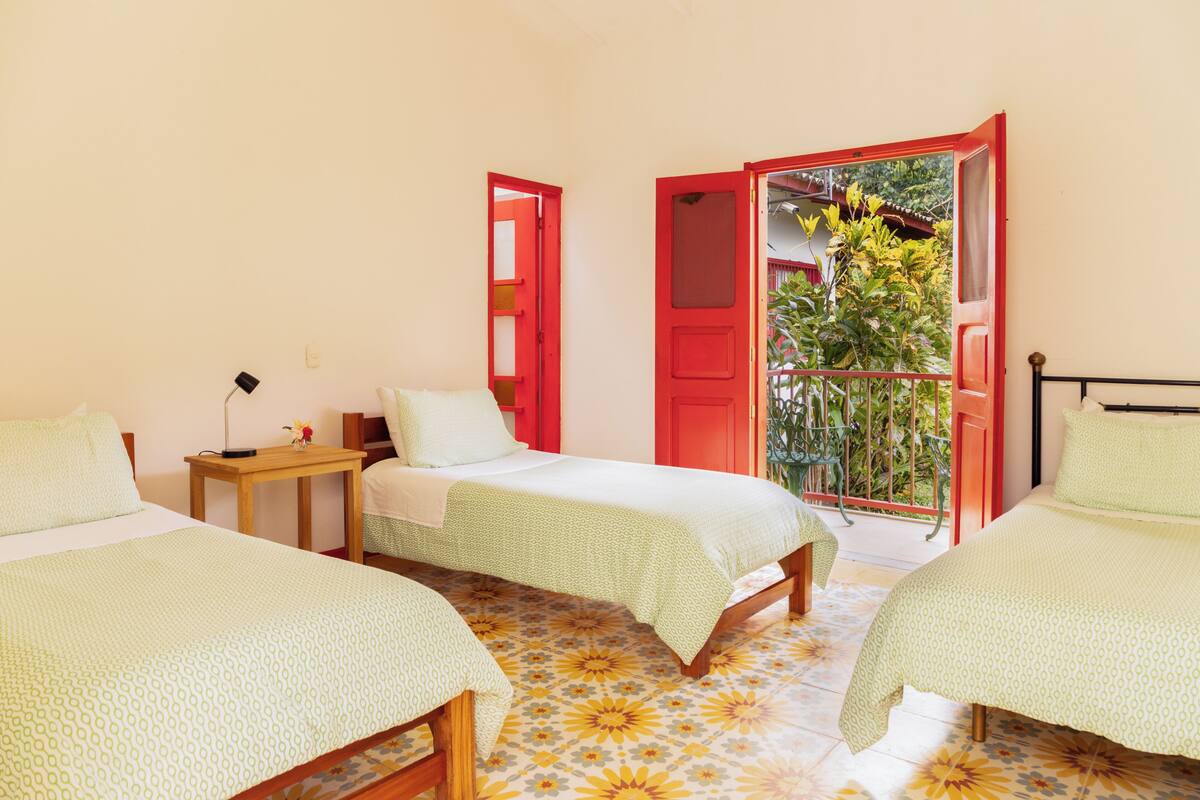 Una habitación con dos camas, una mesita y un balcón con una puerta roja.