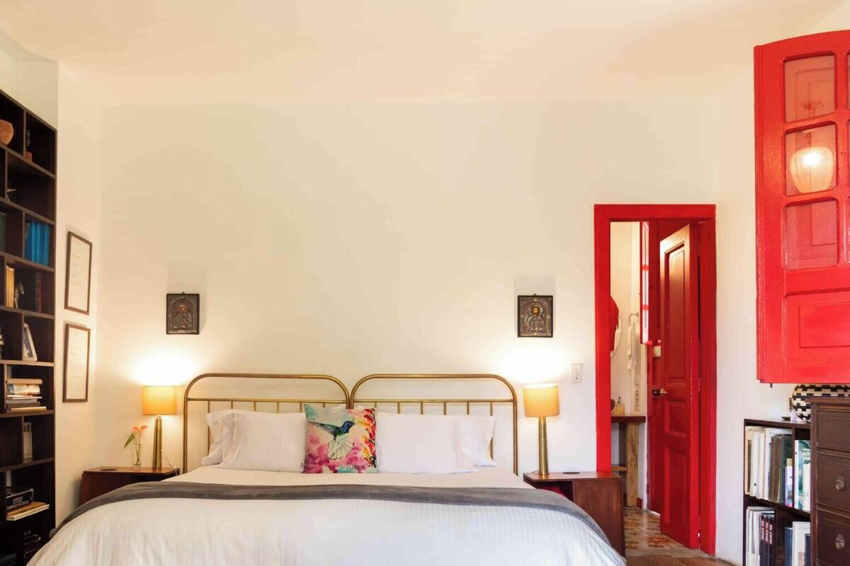 Un dormitorio con una cama, lámparas de noche, una estantería y una puerta roja.