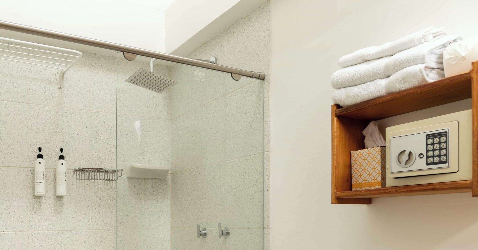 Een douche met een glazen deur, een handdoekhouder en een plank met handdoeken en een kluisje.