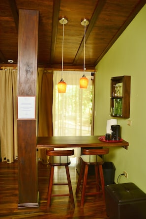 A wooden dining table with two chairs, a hanging light fixture, and a cabinet with glassware. - Finca Vibran Bed and Breakfast (San Isidro de Grecia)