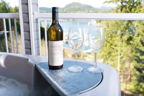 Une bouteille de vin Chaberton Reserve et deux verres sur un balcon donnant sur un lac et des bateaux.