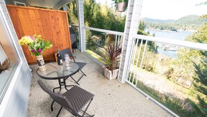 Un balcón con mesa y sillas, un jarrón de flores y vistas a un lago y bosque.