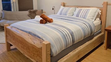 A wooden bed with a striped bedspread and pillows, a rolled towel, and a bedside table.
