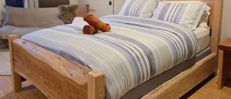 Una cama de madera con colcha a rayas y almohadas, una toalla enrollada y una mesita de noche.