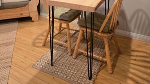 Una habitación acogedora con una mesa de madera, dos sillas, una cama con almohada a rayas y un estante con fotografías.